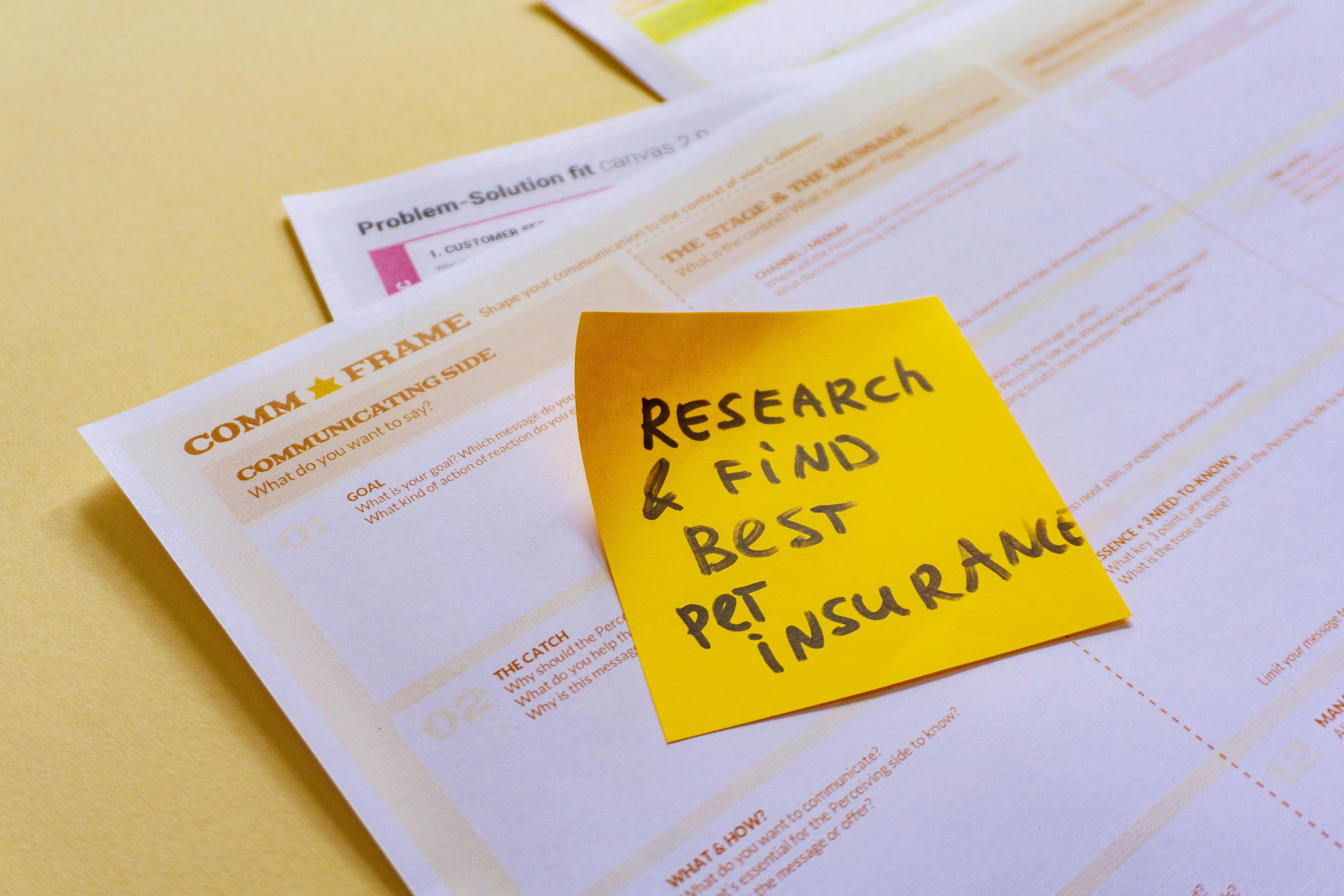 A sticky note saying 'Research & Find Best Pet Insurance' on the top of some papers